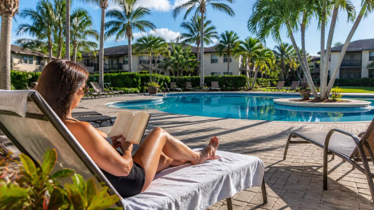 Amenities to Look for in Boca Raton Rentals 2 A resort-style swimming pool framed by palm trees and lounge chairs at a garden-style apartment community in South Florida, with a resident reading on a chaise in late afternoon light