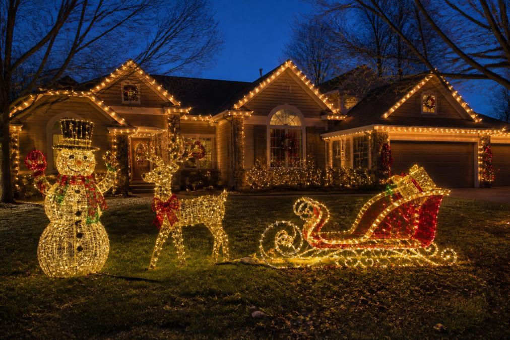 Beautifully illuminated residential home at dusk featuring detailed handcrafted animated outdoor Christmas displays with powder-coated light sculptures creating a festive, magical atmosphere