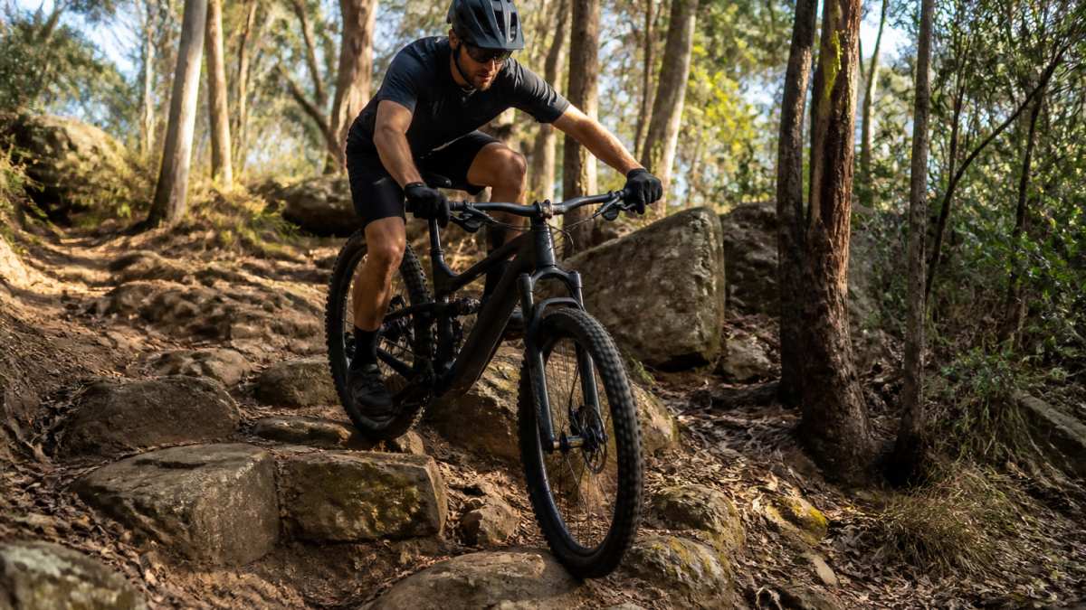 Rider on Amflow PR Carbon Pro navigating technical rocky terrain, demonstrating the mixed-wheel setup's agility through a challenging section with natural forest lighting