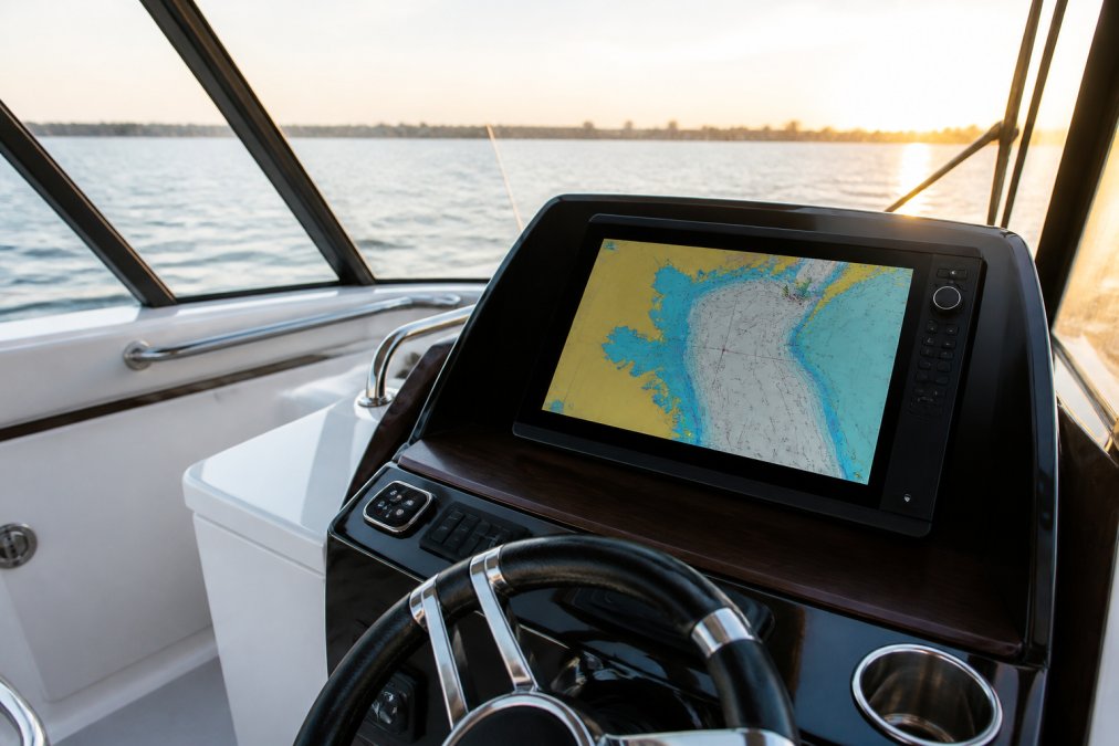 A modern boat helm with a large multi-function chartplotter display mounted at the console, showing a navigation chart, with sunlight visible through the windshield