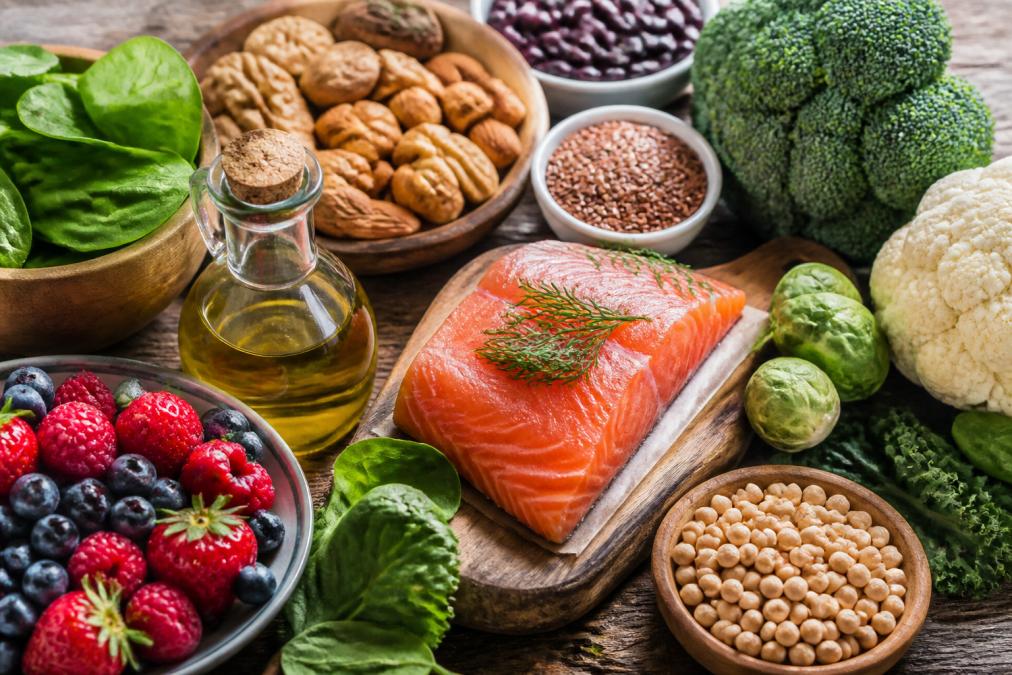 Colorful array of fresh anti-inflammatory foods arranged on a wooden table in natural light: wild salmon fillet, mixed berries, leafy greens, olive oil, nuts, cruciferous vegetables, and legumes in bowls