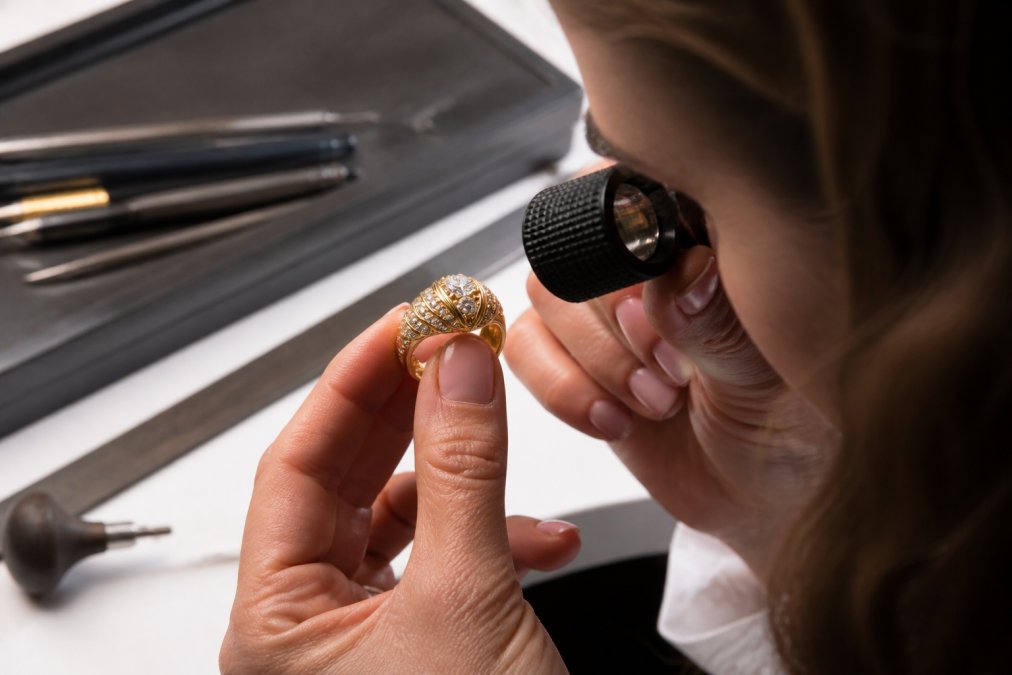 Jeweler's magnified view of antique diamond ring hallmark under gemological loupe, with detailed metal purity stamps visible on white background