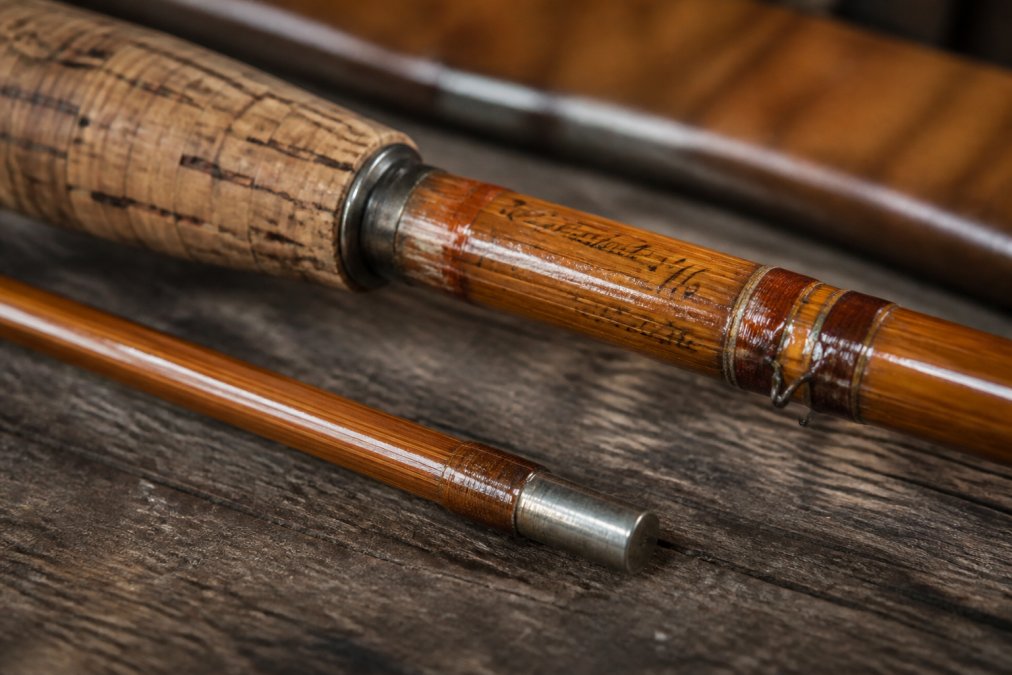 Close-up of antique fly rod showing maker marks, serial numbers, and ferrule details etched into the rod blank near the cork grip