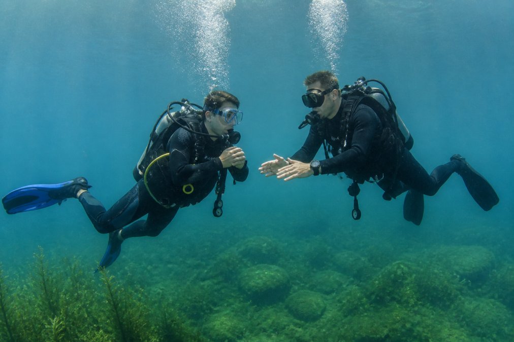 Ein Tauchschüler und sein Tauchlehrer führen während eines Freiwassertauchgangs im klaren Wasser des Bodensees eine Übung zur Auftriebskontrolle durch. Beide tragen eine vollständige Tauchausrüstung, der Schüler zeigt eine entspannte und konzentrierte Haltung.