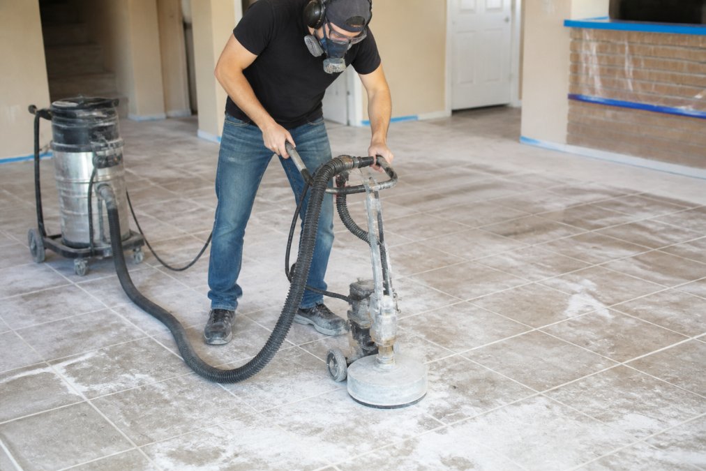 Professional using diamond grinding equipment on tile surface with dust containment, showing mechanical abrasion technique in action with proper safety equipment