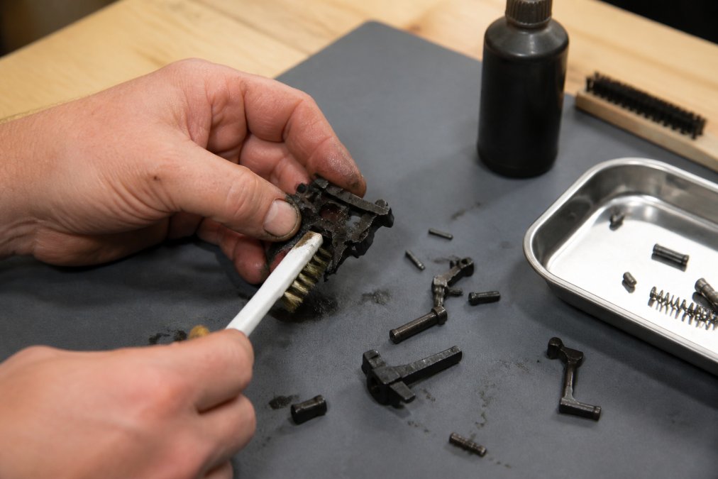 Hands scrubbing carbon from an AR-15 trigger group during cleaning
