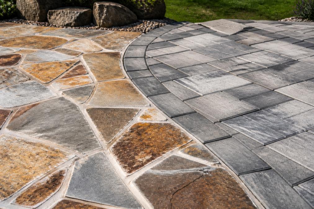 Close-up of natural stone flagstone patio surface next to concrete pavers in a residential backyard, showing color variations and texture differences in afternoon sunlight