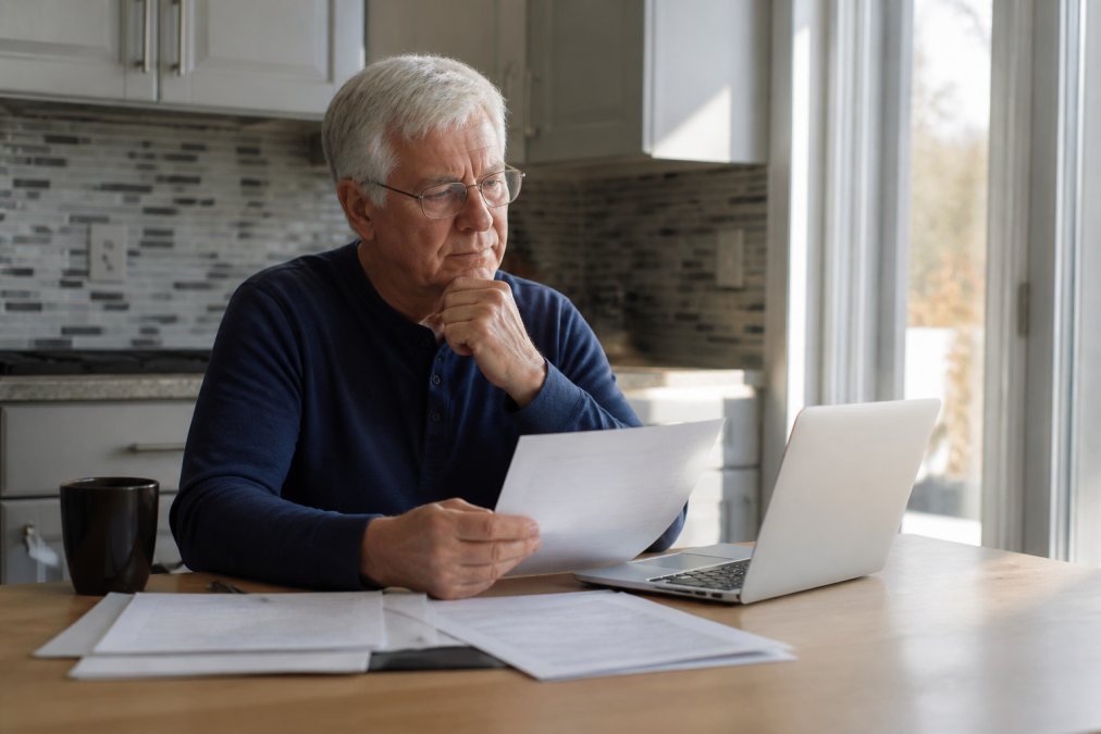 Senior reviewing zero premium Medicare Advantage plan documents and digital options on a laptop at a kitchen table