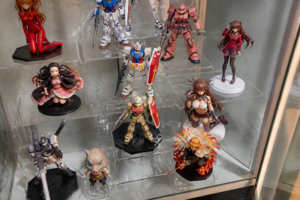 A detailed overhead view of an acrylic riser arrangement showing multiple anime figures and Gundam models positioned at varying heights with intentional spacing, demonstrating visual hierarchy and depth on a collector's shelf