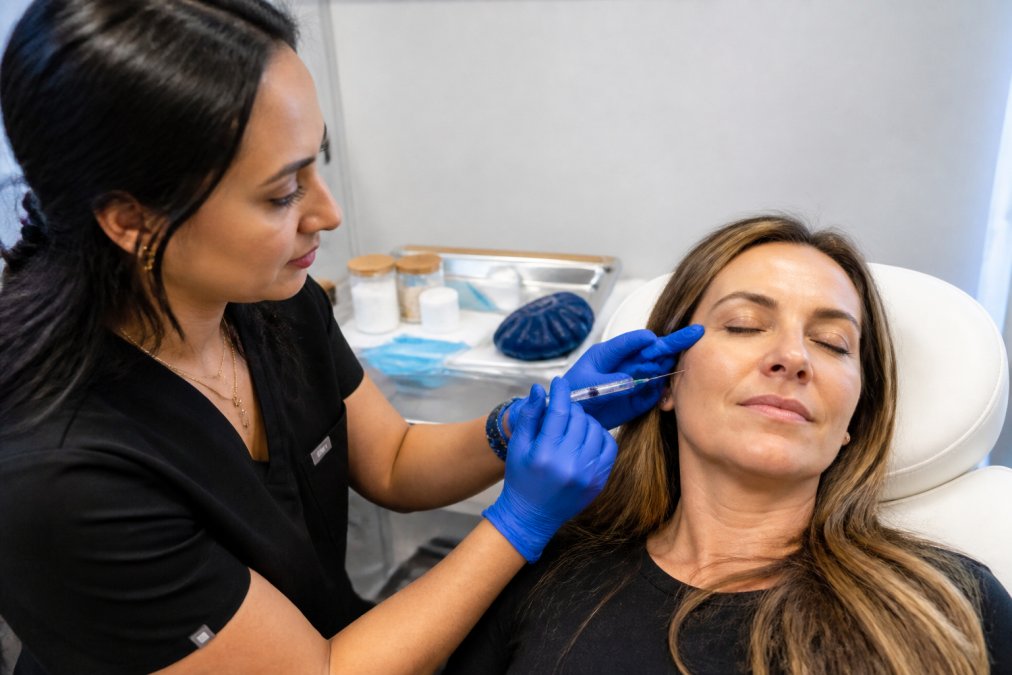 Professional demonstrating aesthetic injectable technique in modern clinical setting with fine-gauge needle, ice pack, and numbing cream on tray
