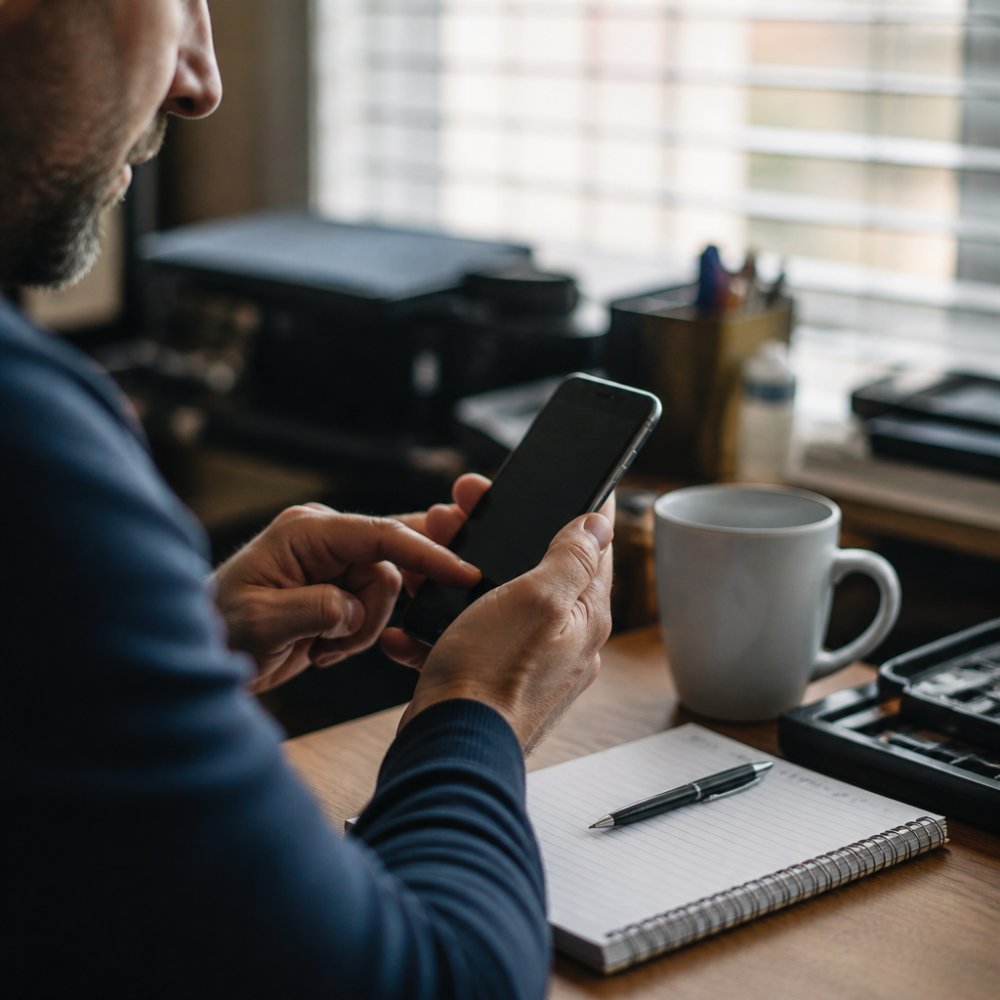 A plumbing company owner in a dimly lit home office at night, phone screen glowing as an automated call summary appears, expression relieved
