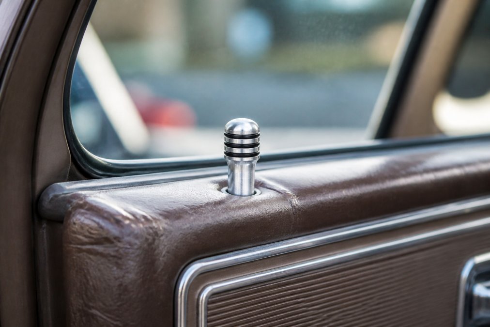 Close-up of machined billet aluminum door lock knobs with 3-band design installed on a classic truck door panel, showing the contrast between shiny billet finish and weathered interior trim