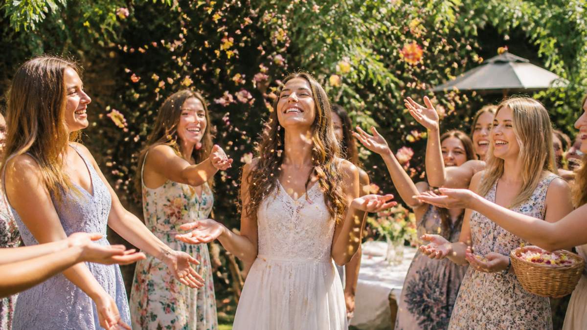 Bride and guests tossing colorful biodegradable confetti made of dried flower petals in a sunlit garden