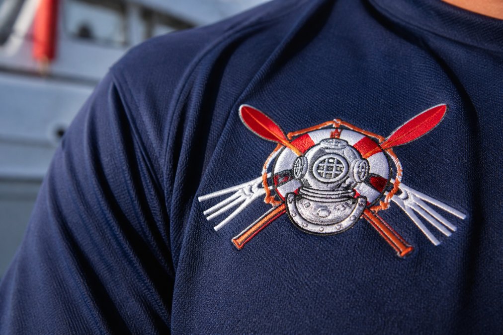 Close-up of embroidered rescue swimmer insignia on dark navy poly fabric, showing detailed thread work and print clarity with professional lighting