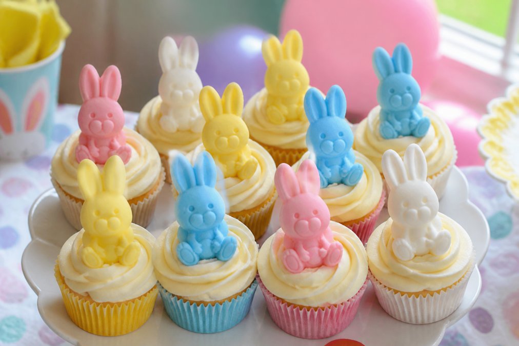 Colourful handmade edible sugar paste toppers in various designs and colours arranged on decorated cupcakes at a children's birthday party, showing diverse character and shape designs
