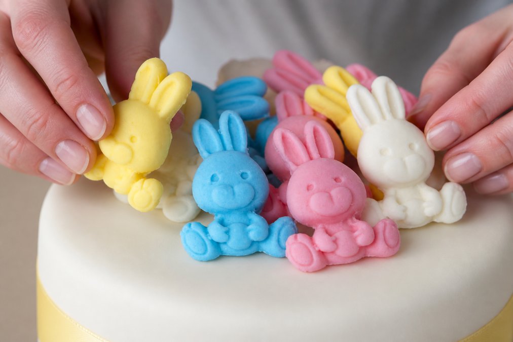 Close-up of hands carefully placing edible sugar paste decorations onto a cake surface with proper technique, showing secure attachment and careful positioning
