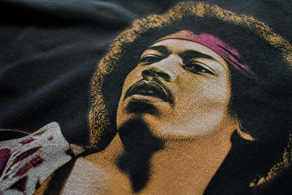 Close-up of a high-quality band tee showing detailed screen print texture with crisp ink lines, precise color registration, and visible cotton weave through lighter ink areas under natural window lighting