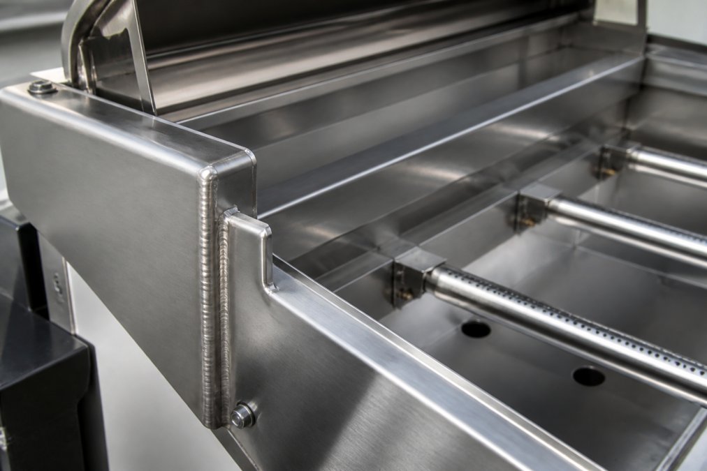 Close-up of welded stainless steel grill construction showing heavy-gauge material thickness, burner assembly, and precision welding on a premium grill