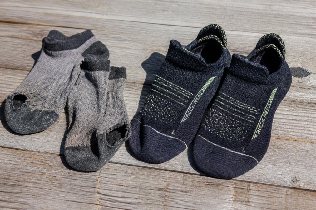 Close-up of worn-out budget socks with visible holes, fraying seams, and faded color next to pristine premium athletic socks showing tight weave and vibrant fabric