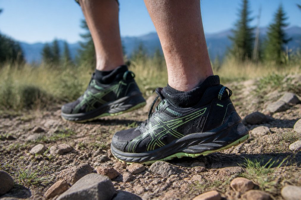 Trail runner's feet in high-performance hiking socks during an outdoor run on rocky, debris-strewn terrain, showing the sock's snug fit and protective design in action