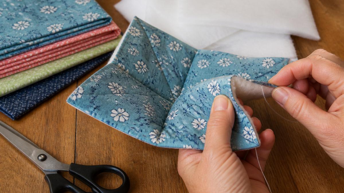 Detailed step-by-step process of hand-stitching cotton fabric layers to construct a microwave-safe bowl cozy.