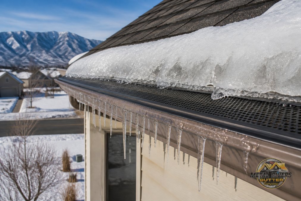 Diagram showing how gutter guards prevent ice dam buildup on a snowy roofline during winter conditions.