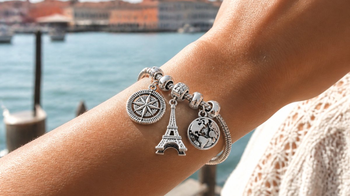 Close-up of a sterling silver charm bracelet with travel-themed charms including Eiffel Tower, compass, and world map designs displayed on a woman's wrist in natural sunlight
