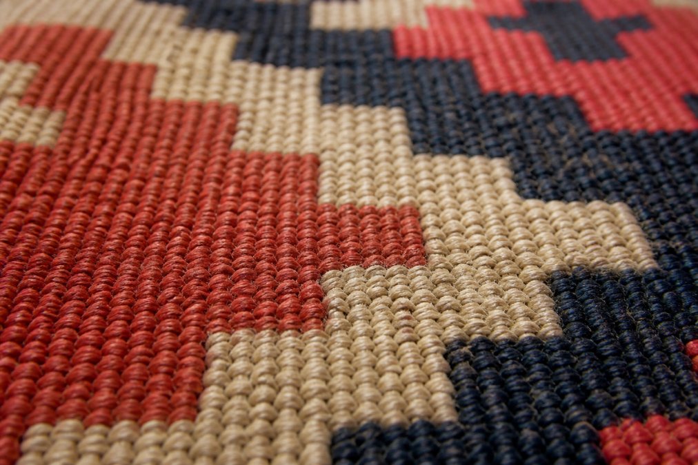 Close-up of a handwoven kilim rug's flatweave textile structure showing the interlocking warp and weft threads, with natural light highlighting the fiber density and weaving technique