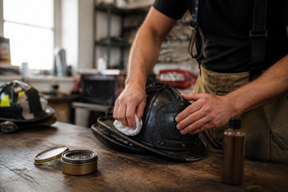 Professional firefighter's hands carefully conditioning a leather fire helmet with quality leather care products on a workbench with natural lighting