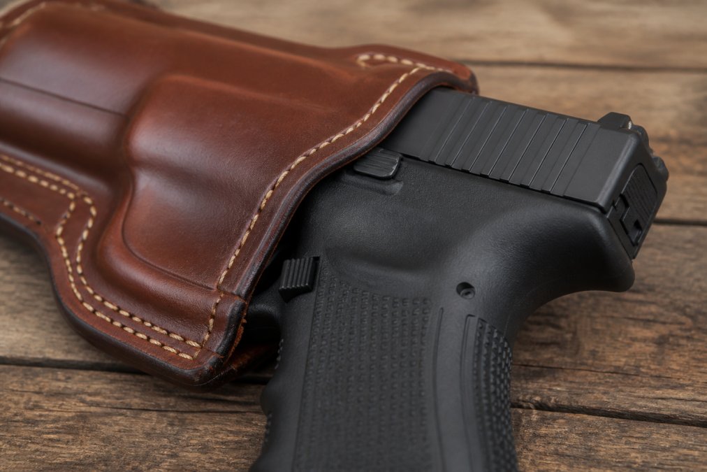 Close-up of a leather holster's reinforced mouth showing the molded trigger guard area with a polymer-framed striker-fired pistol partially inserted, demonstrating proper fit and retention