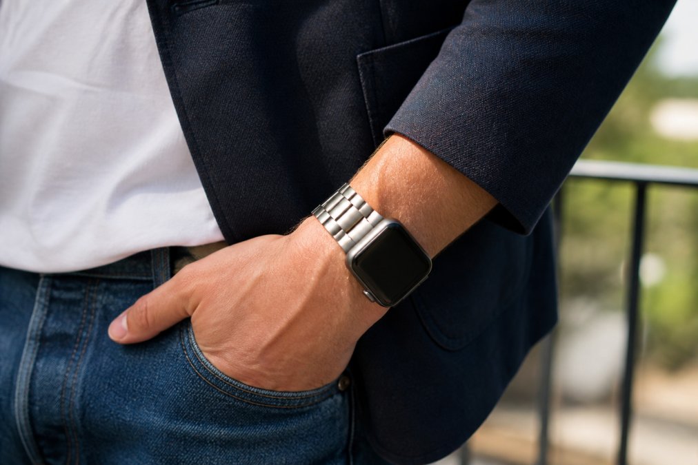 Brushed stainless steel link watch band worn with a casual blazer and jeans in natural daylight