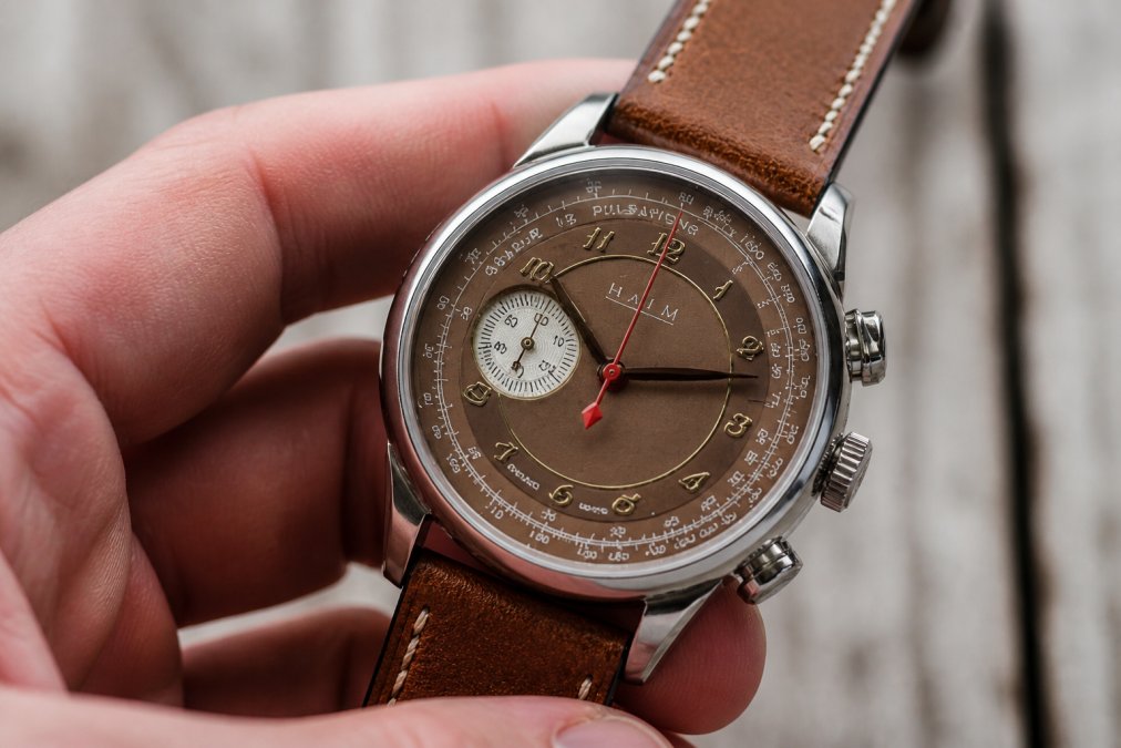 Close-up of a hand-finished titanium watch case with ornate dial decoration visible through sapphire crystal, showing intricate case finishing and numerals under soft studio lighting