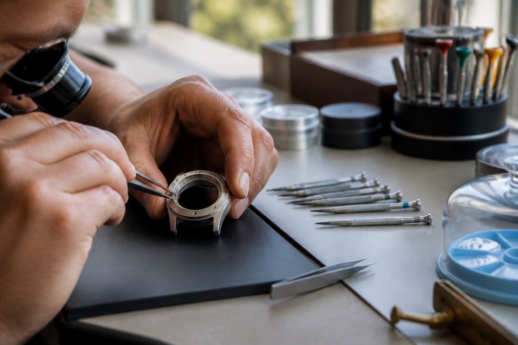 Watchmaker assembling a titanium case for microbrand watches using precision tools on a sunlit workbench