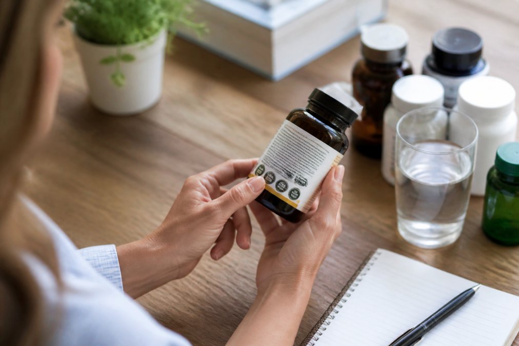 Close-up of hands examining a supplement bottle label and third-party certification seal in natural daylight