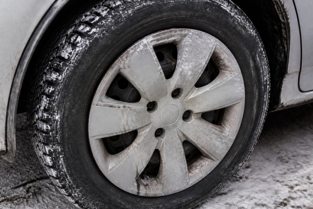 Close-up of a vehicle wheel showing visible road salt residue, brake dust accumulation, and weathering marks on a plastic wheel skin during winter driving conditions