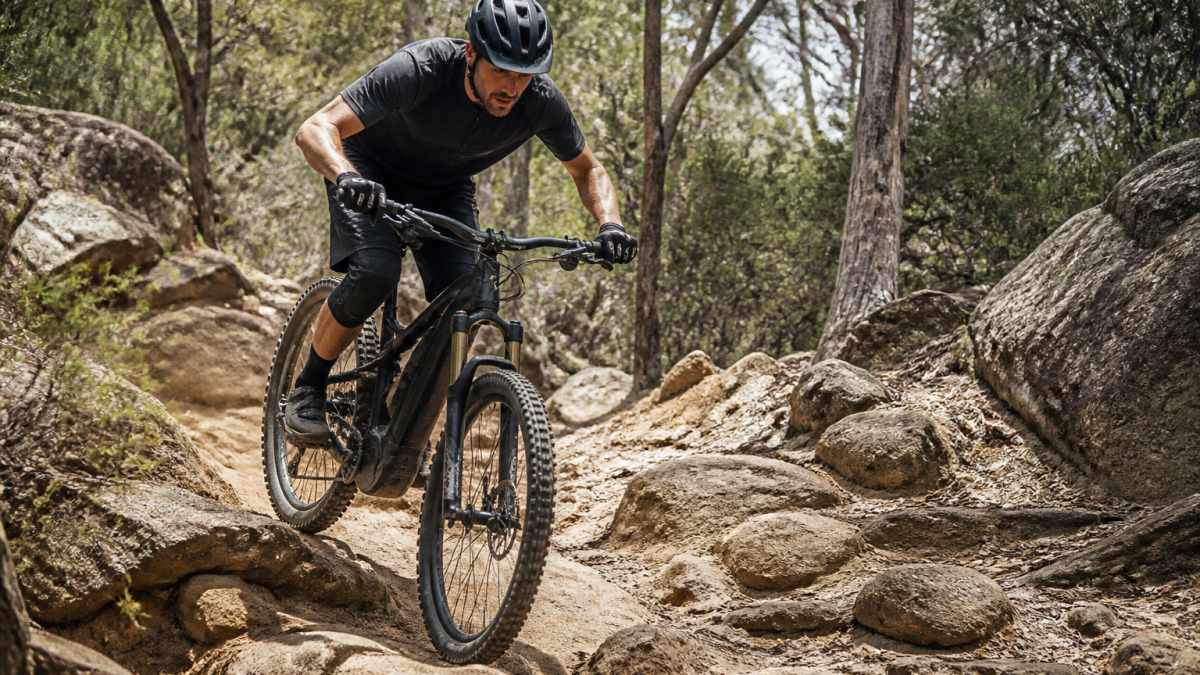 Rider navigating technical rocky terrain on a high-spec premium e-MTB, demonstrating suspension performance and control on steep singletrack with natural trail lighting