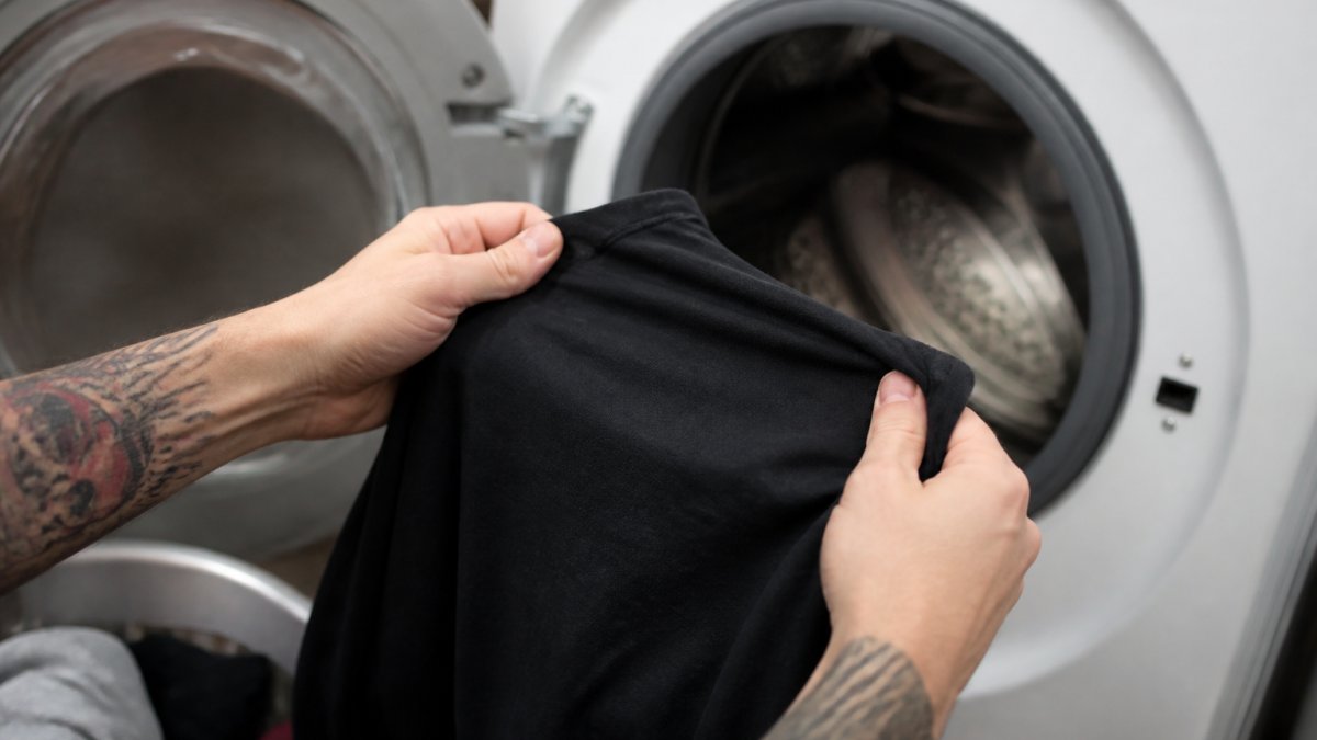 Close-up of hands turning a black graphic t-shirt inside out before placing it in a washing machine, showing proper care technique