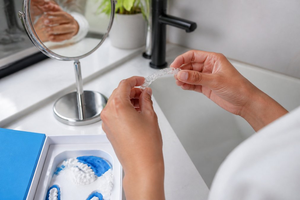 Person holding a custom snap on veneers tray above a bathroom sink with a dental mould kit nearby