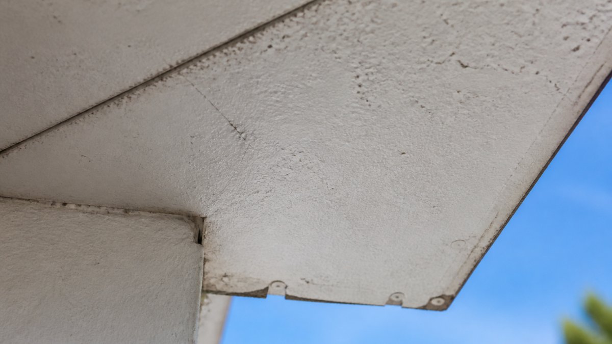 Infographic identifying visual signs of asbestos soffits like dimpled textures, hairline cracks, and edge chips.