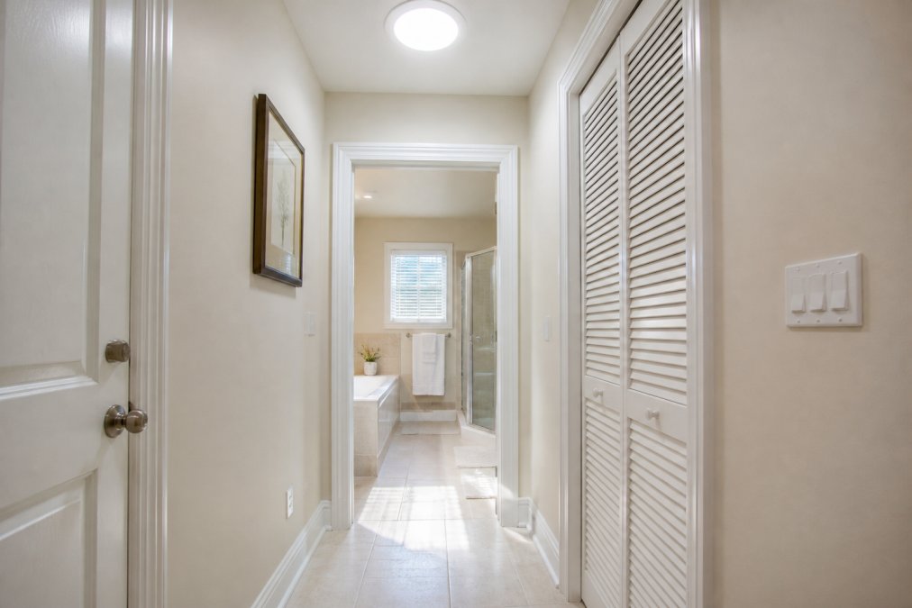 A bright hallway and bathroom interior lit entirely by natural daylight from a ceiling diffuser, no lamps switched on, warm sunlight falling across the floor and walls