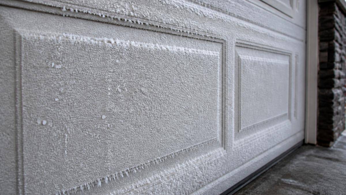 Close-up of a vinyl garage door panel showing frost buildup and condensation in winter conditions, with visible ice crystals forming on the surface and edge seams
