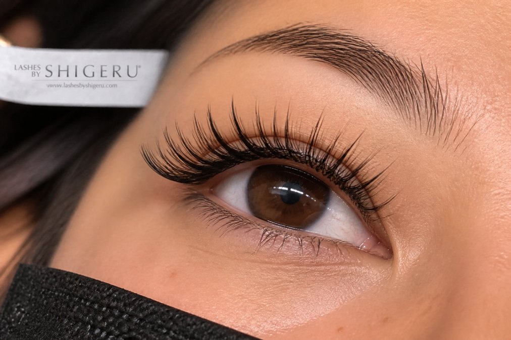 Close-up of a client's eye with freshly applied weightless lash extensions showing feathery, natural appearance with individual lash definition against natural lashes in professional studio lighting