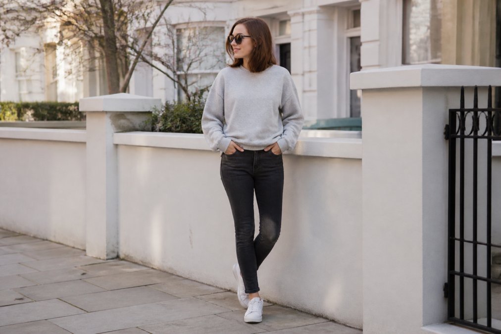 Person wearing a witty slogan sweater styled casually with fitted dark jeans and white trainers, standing in relaxed pose in natural daylight