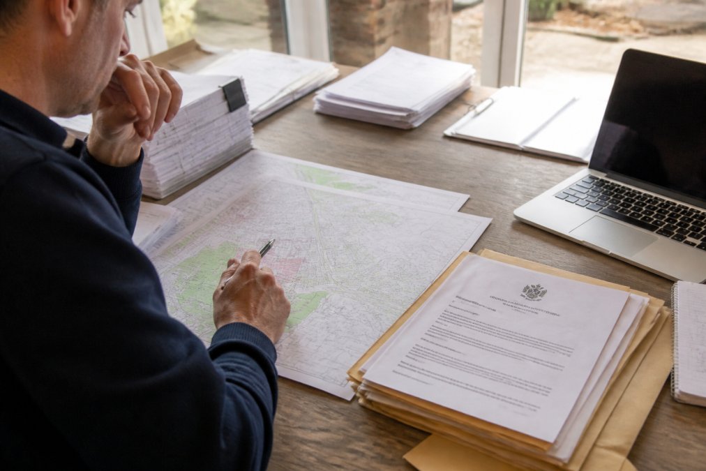 Property owner or landlord reviewing planning documents and maps on a desk with a laptop, planning permission forms, and local authority notices visible