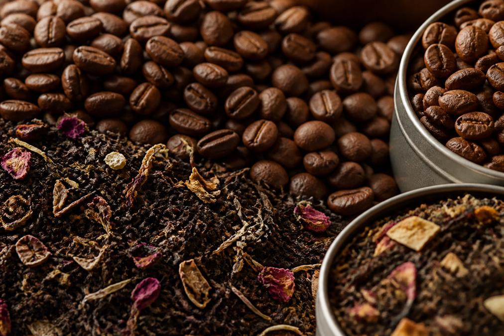 Close-up of artisan coffee beans in rich brown tones and loose-leaf tea leaves showing varied colors and textures, arranged together with natural light highlighting the quality and freshness of specialty-grade ingredients