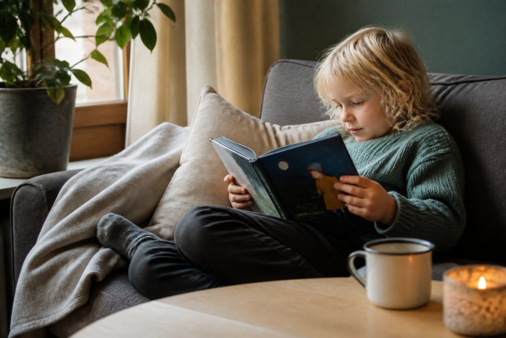 Barn som leser emosjonelle barnebøker alene på en koselig sofa med pute og viser stort engasjement for historien.