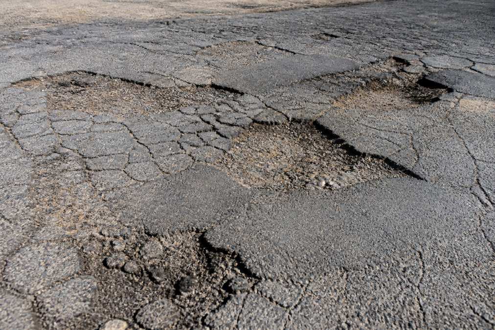 Close-up of severely damaged asphalt driveway showing alligator cracking, multiple potholes, and extensive surface deterioration in bright daylight