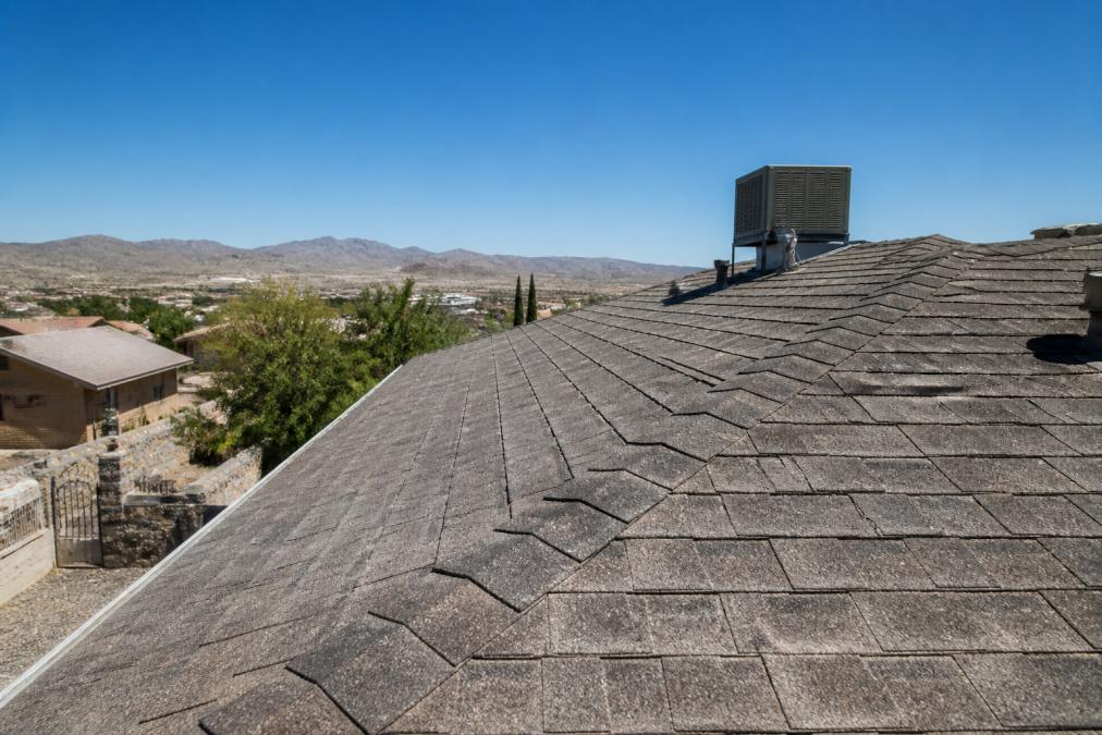 Residential roof installed with asphalt shingles under bright desert sun, showing heat reflection and dust accumulation on the surface with clear blue sky overhead