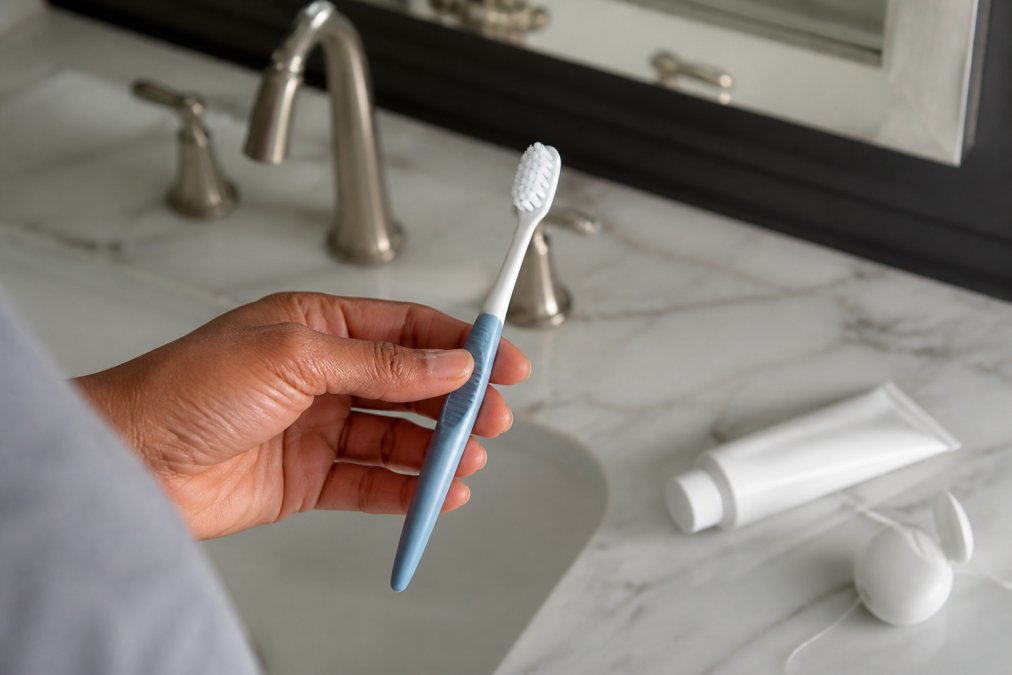 Person holding a soft-bristled toothbrush near toothpaste and floss to treat receding gums