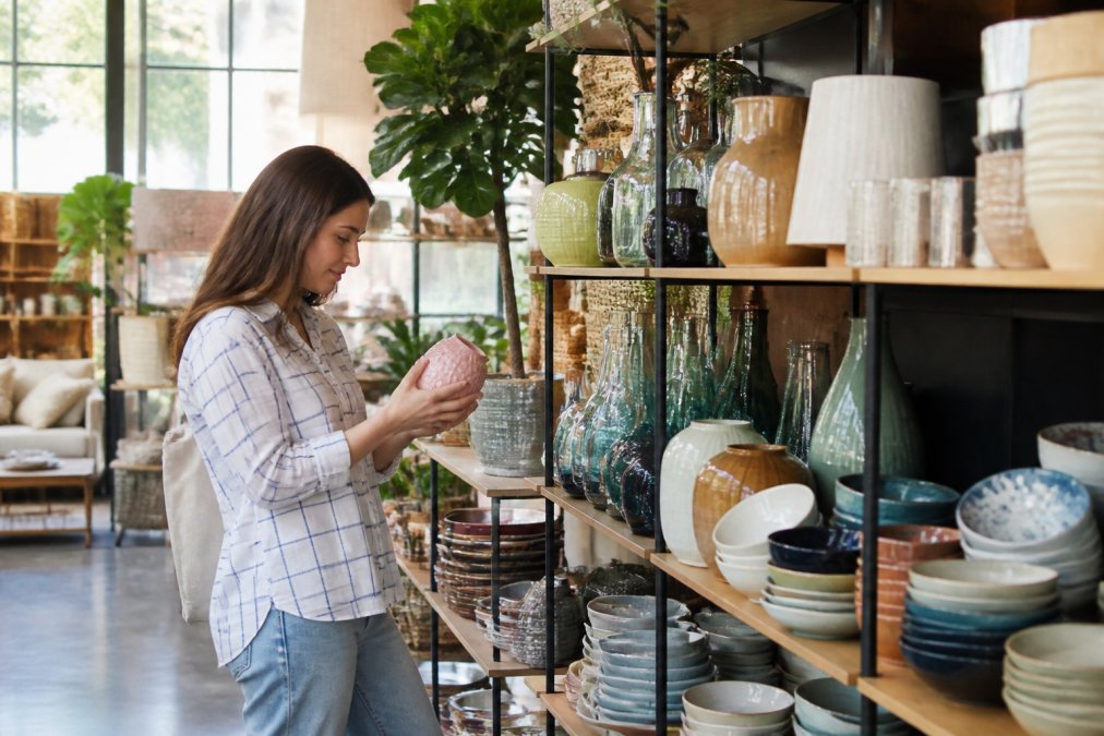 Customer browsing shelves of colorful home décor items, dishware, and serveware in a bright retail store with natural lighting streaming through large windows